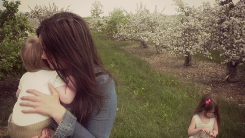 mother holding baby with toddler behind her in an orchard